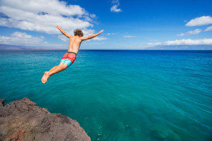 Man jumping off cliff into the ocean. Summer fun lifestyle.